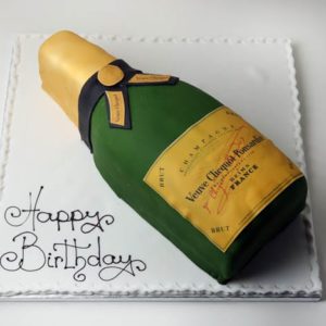 A champagne themed birthday cake in the shape of a champagne bottle with icing detailing