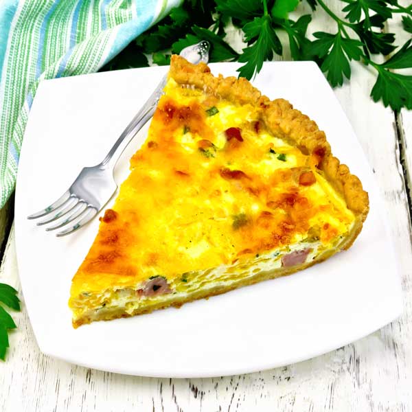 A slice of quiche on a white plate with a fork from Quigleys cafe, bakery and deli