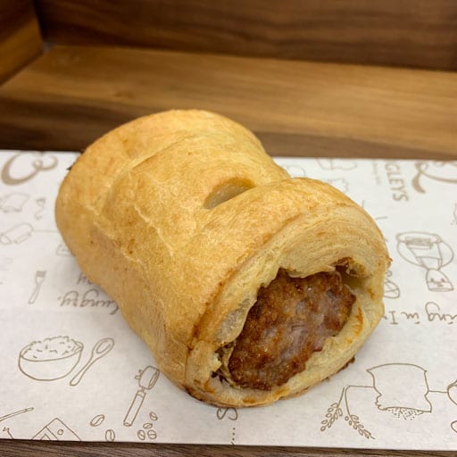 A sausage roll displaued on white paper from Quigleys cafe, bakery and deli
