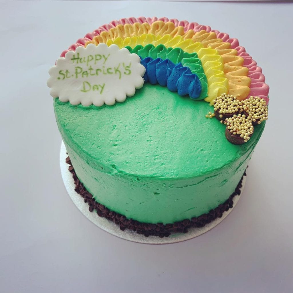A green Saint Patricks Day themed cake with rainbow icing detailing by Quigleys bakery